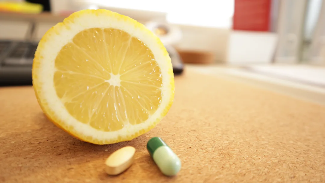 Imagem de um limão cortado ao meio com uma drageia de um suplemento de vitamina C natural e com outra drageia de um suplemento sintético
